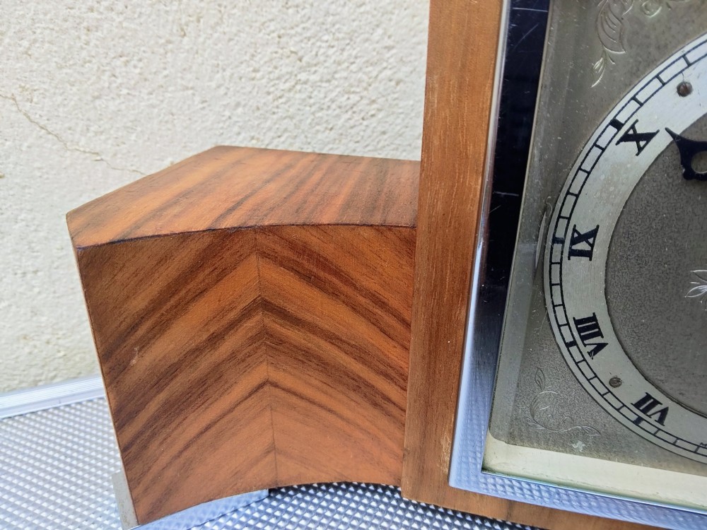 An Art Deco walnut mantel clock featuring chevron-patterned wooden wings, a central square face with Roman numerals, and chrome trim accents. View IV