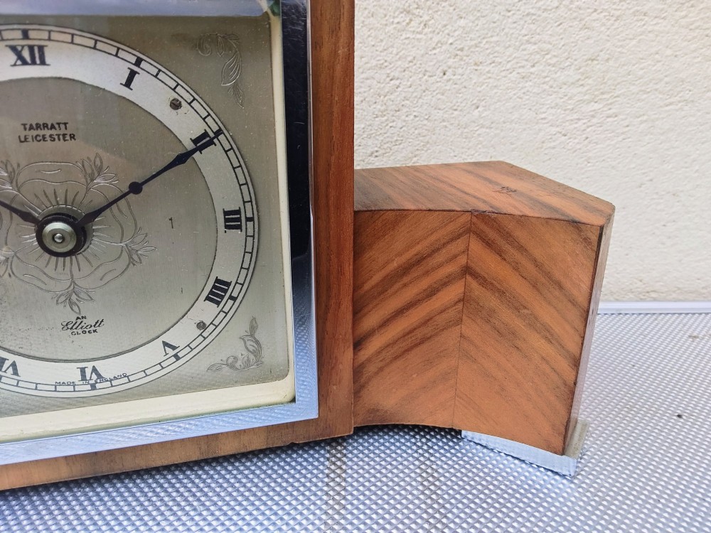 An Art Deco walnut mantel clock featuring chevron-patterned wooden wings, a central square face with Roman numerals, and chrome trim accents. View V