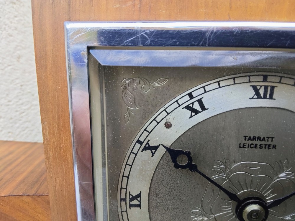 An Art Deco walnut mantel clock featuring chevron-patterned wooden wings, a central square face with Roman numerals, and chrome trim accents. View VII