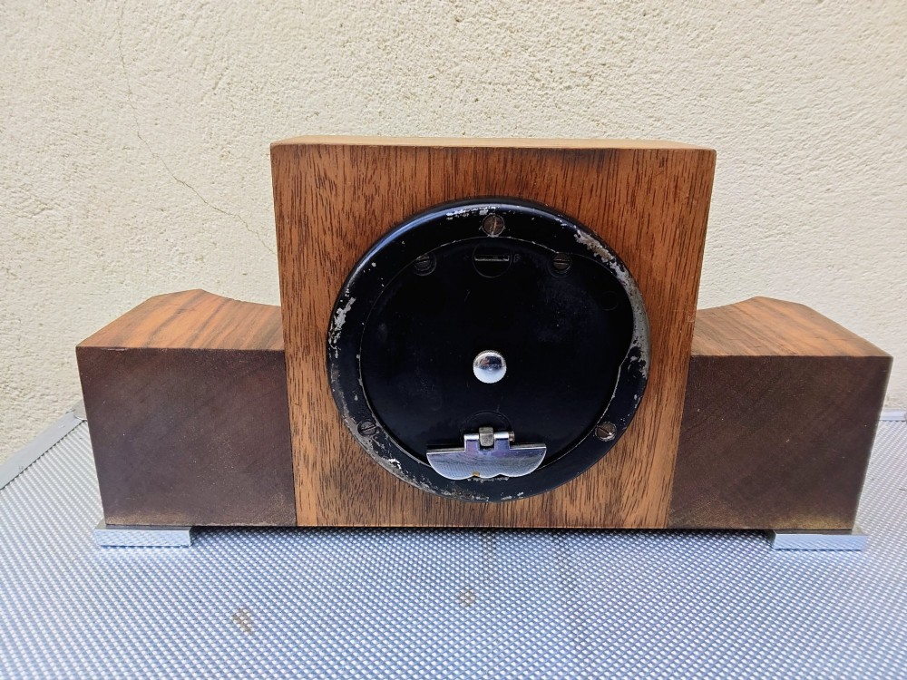 An Art Deco walnut mantel clock featuring chevron-patterned wooden wings, a central square face with Roman numerals, and chrome trim accents. View VIII