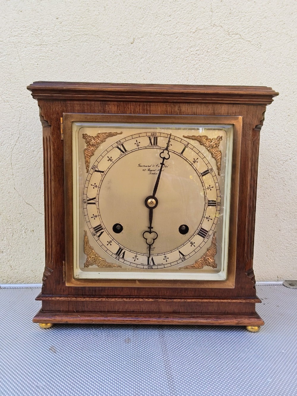 A square mahogany mantel clock featuring fluted side pilasters, brass bun feet, and a silvered dial with Roman numerals and corner brass spandrels.