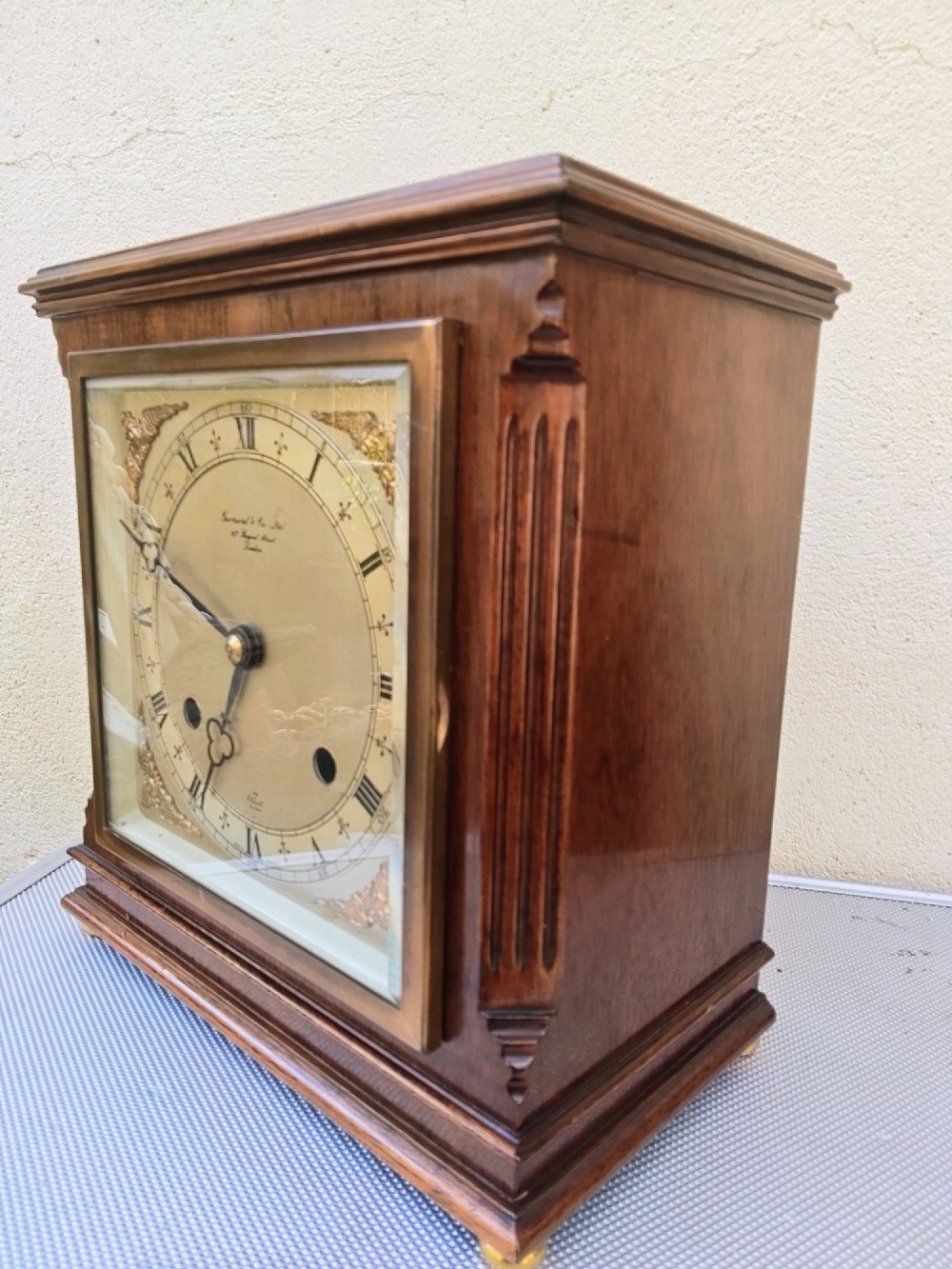 A square mahogany mantel clock featuring fluted side pilasters, brass bun feet, and a silvered dial with Roman numerals and corner brass spandrels. View II