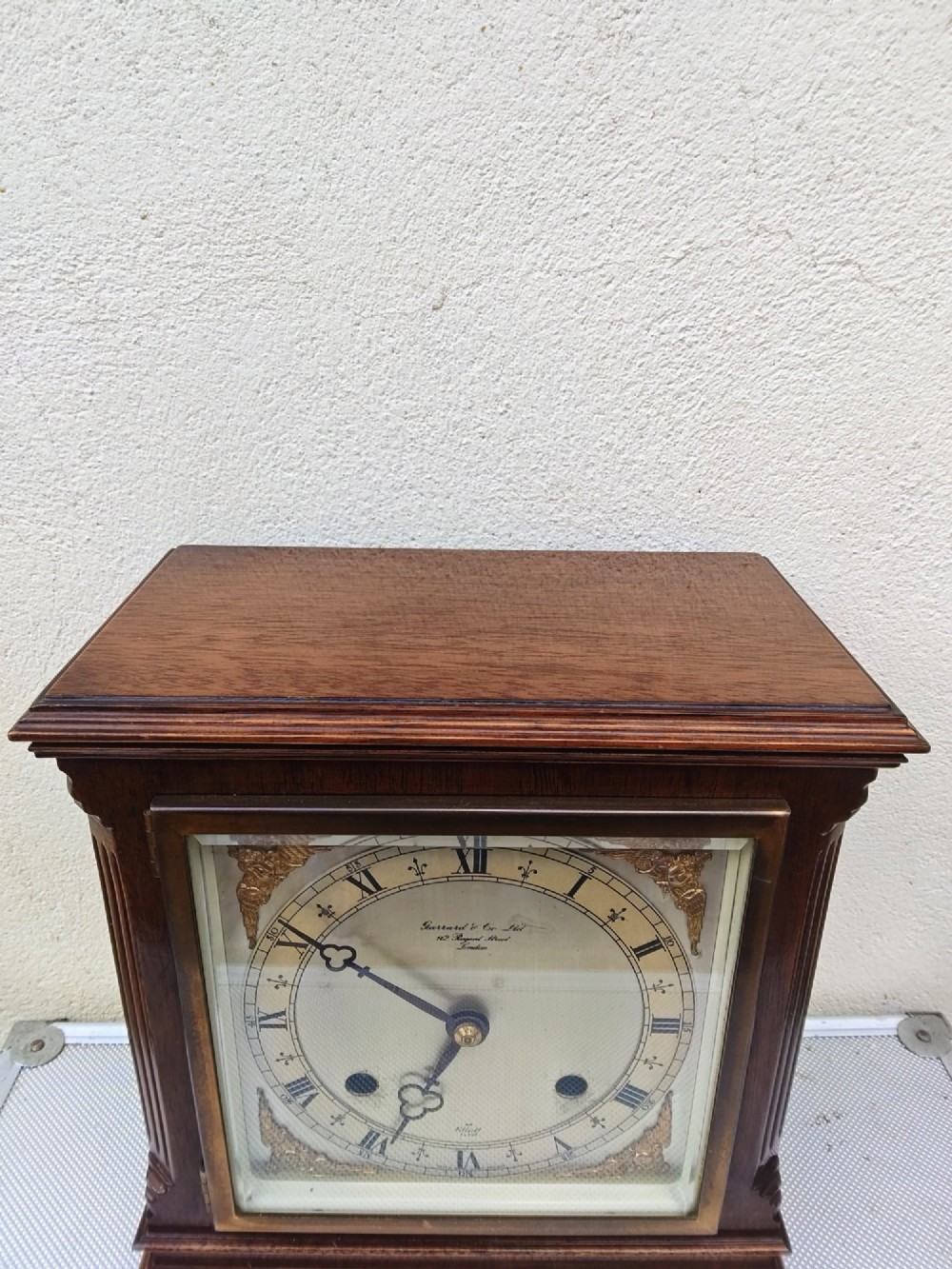 A square mahogany mantel clock featuring fluted side pilasters, brass bun feet, and a silvered dial with Roman numerals and corner brass spandrels. View III