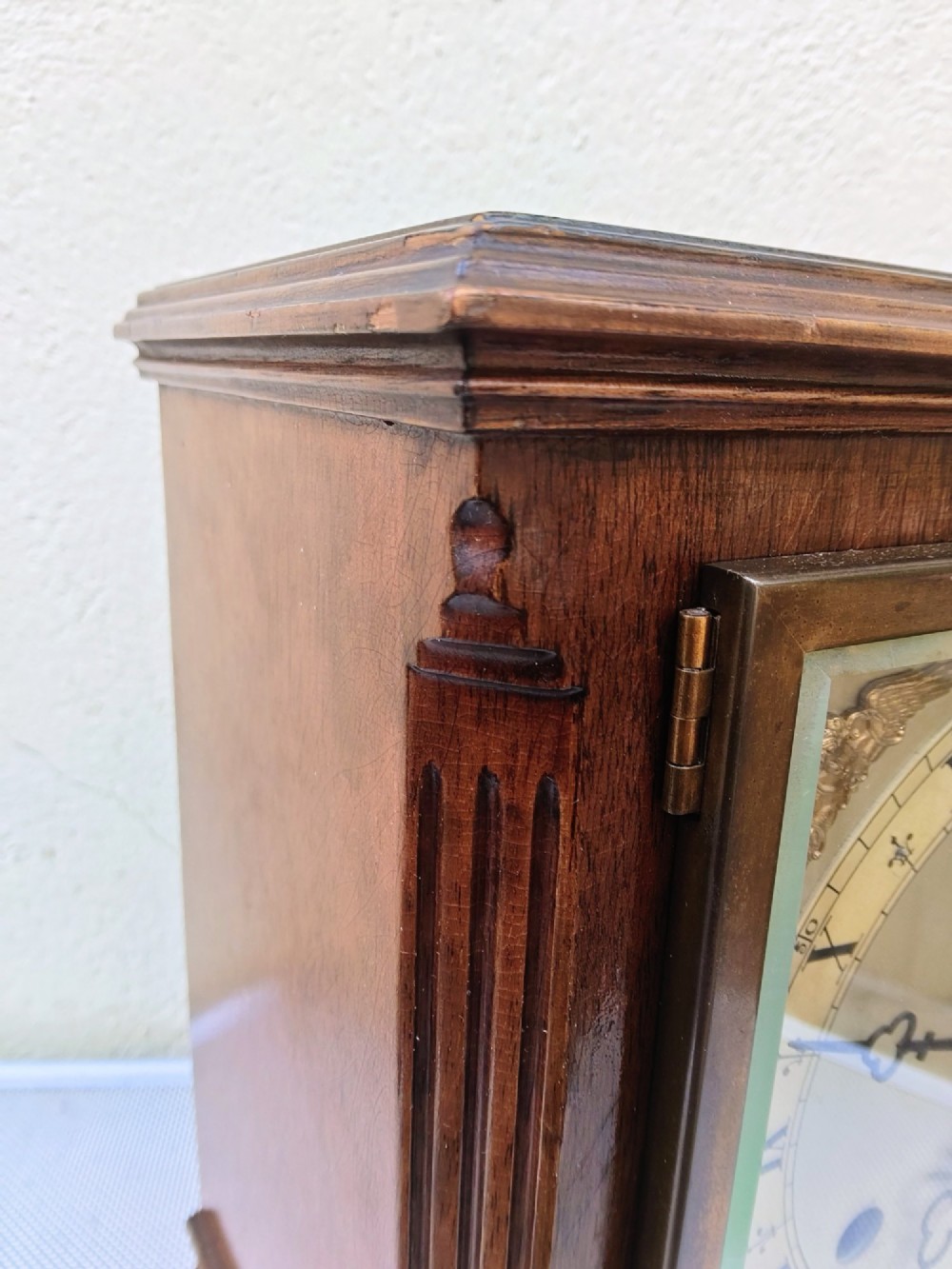 A square mahogany mantel clock featuring fluted side pilasters, brass bun feet, and a silvered dial with Roman numerals and corner brass spandrels. View VI
