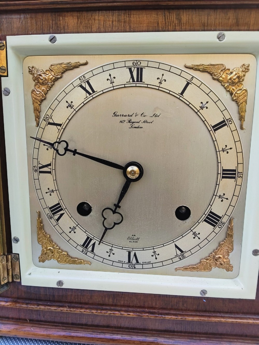 A square mahogany mantel clock featuring fluted side pilasters, brass bun feet, and a silvered dial with Roman numerals and corner brass spandrels. View VIII