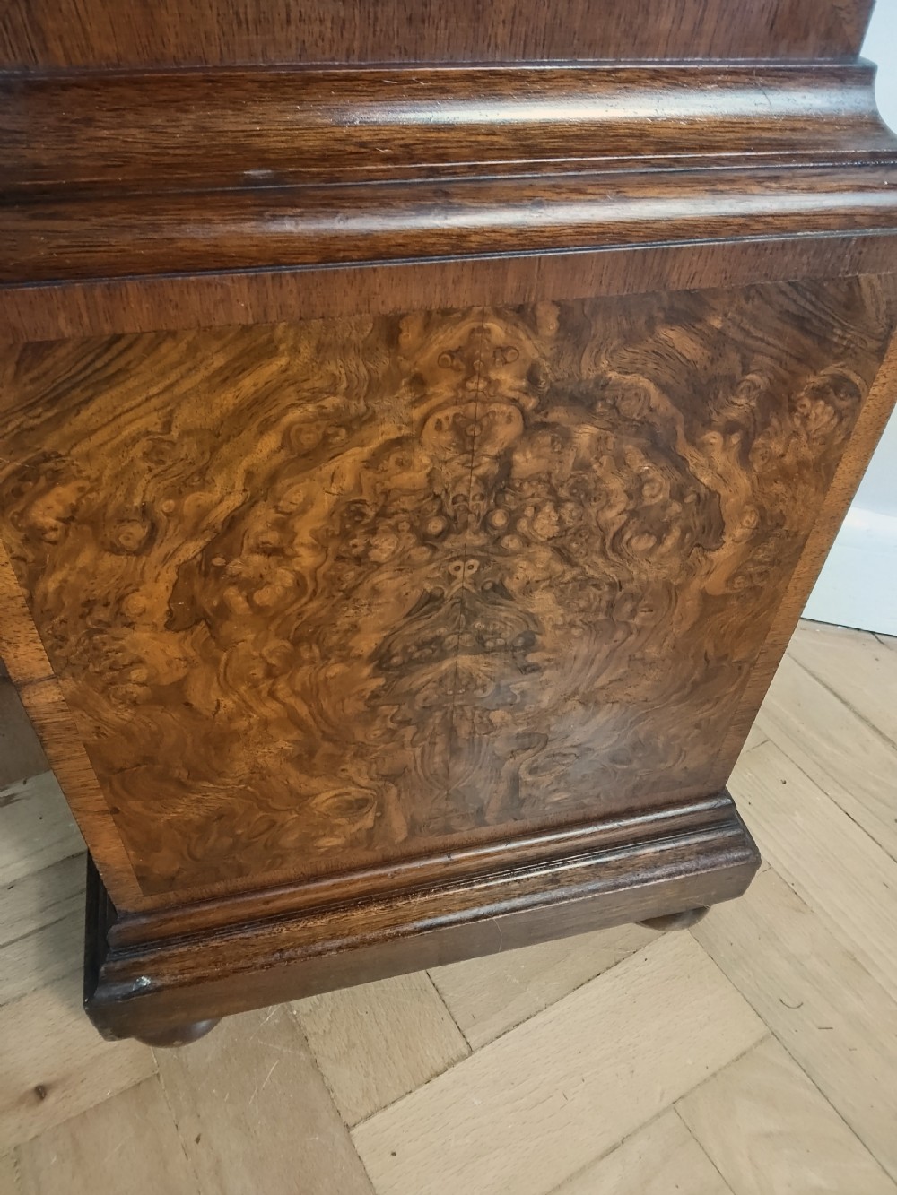 A floor-standing burr walnut grandmother longcase clock featuring a square brass dial, decorative corner spandrels, a coved top with metal finials, and a slender veneered trunk door. View III