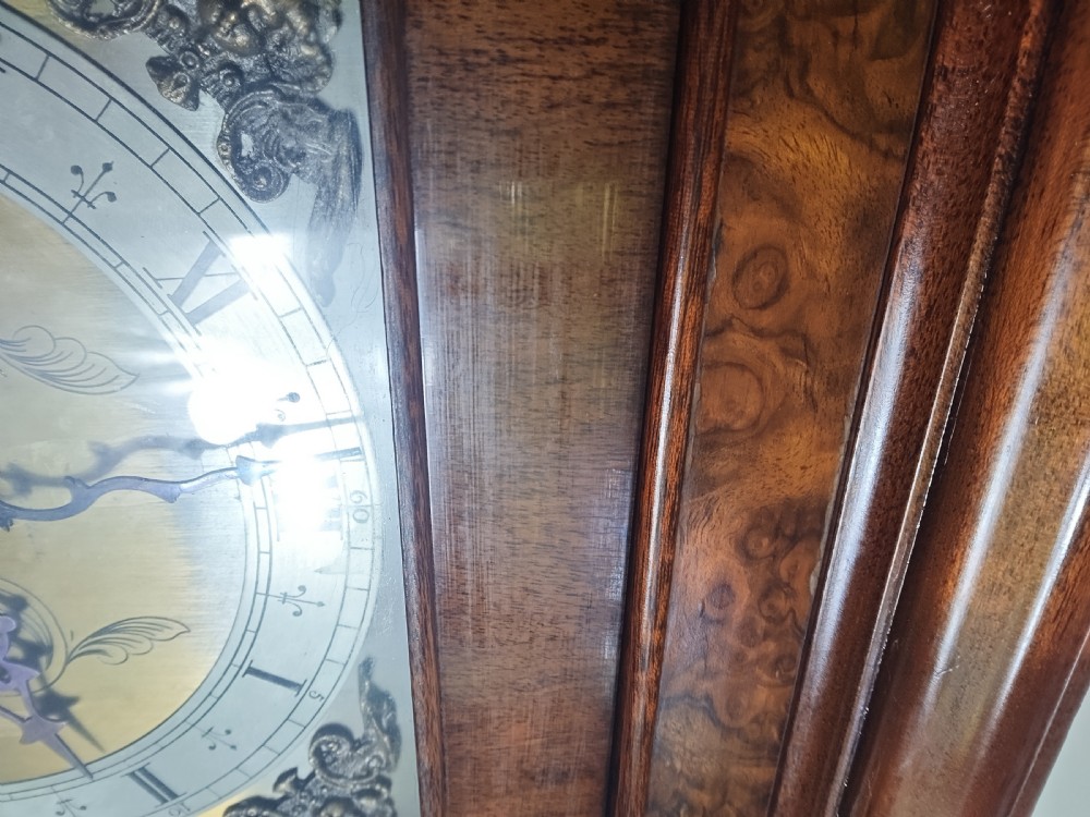 A floor-standing burr walnut grandmother longcase clock featuring a square brass dial, decorative corner spandrels, a coved top with metal finials, and a slender veneered trunk door. View V