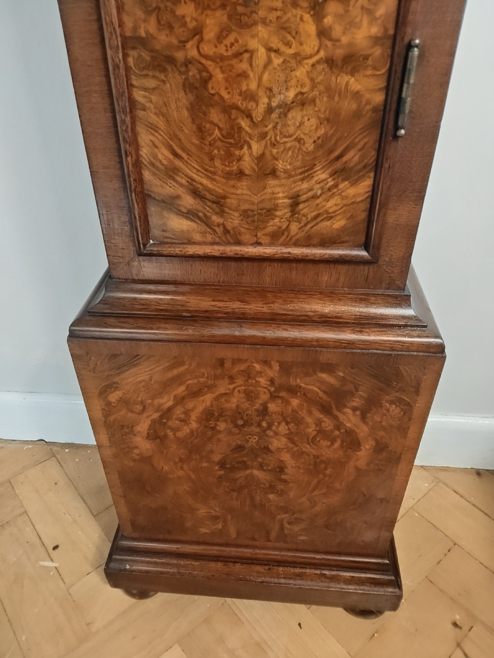 A floor-standing burr walnut grandmother longcase clock featuring a square brass dial, decorative corner spandrels, a coved top with metal finials, and a slender veneered trunk door. View VIII