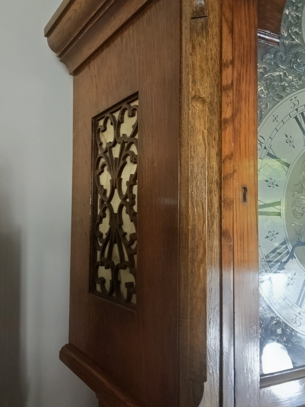 A freestanding wooden longcase clock featuring an arched hood, a brass and silvered dial, and a glazed trunk door revealing weights and a pendulum. View III