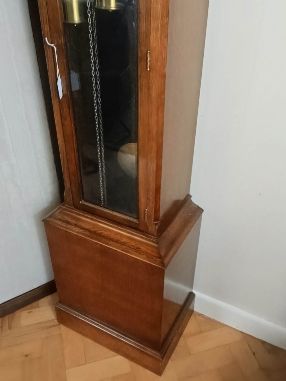 A freestanding wooden longcase clock featuring an arched hood, a brass and silvered dial, and a glazed trunk door revealing weights and a pendulum. View VII