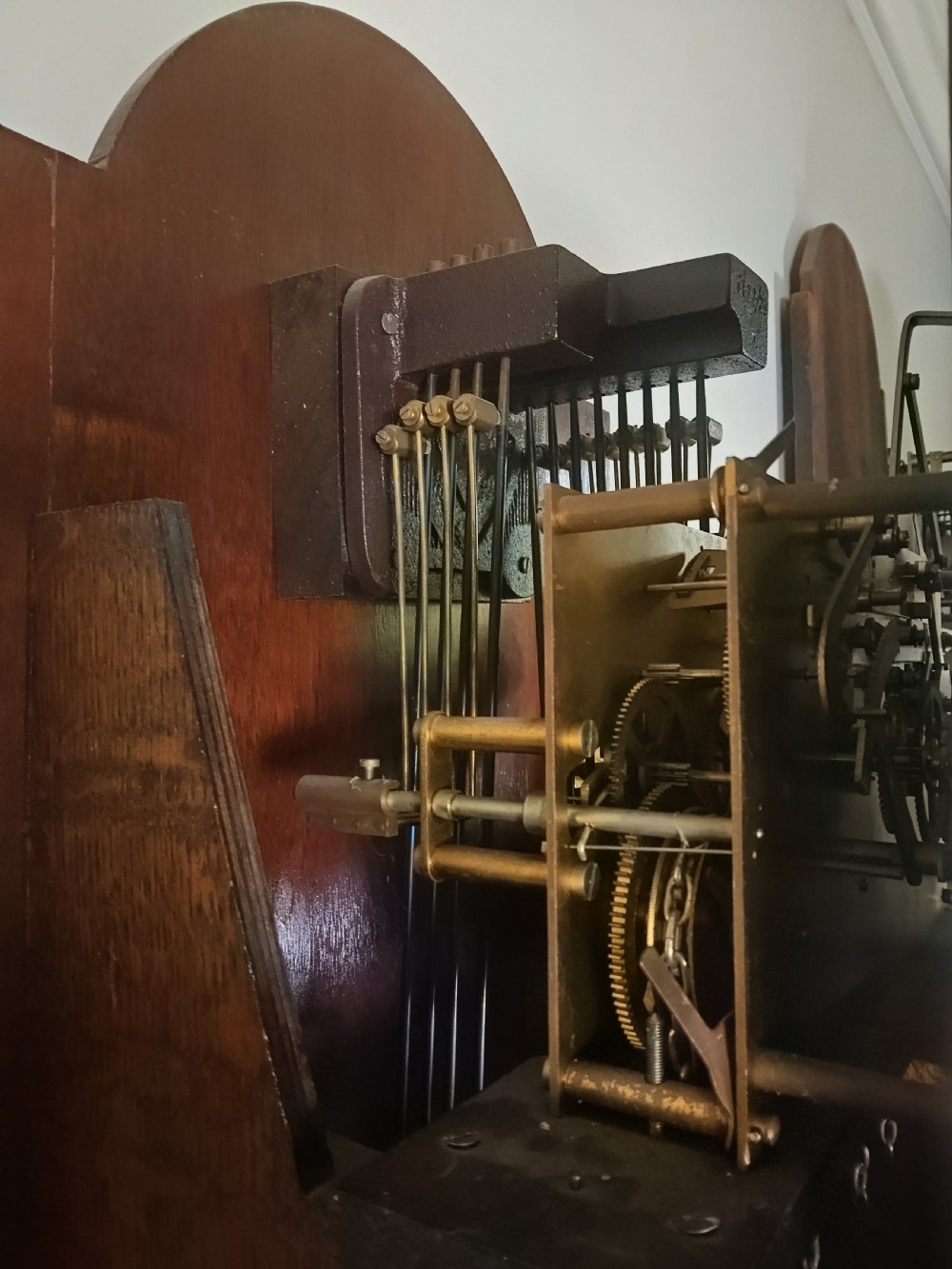 A freestanding wooden longcase clock featuring an arched hood, a brass and silvered dial, and a glazed trunk door revealing weights and a pendulum. View XI