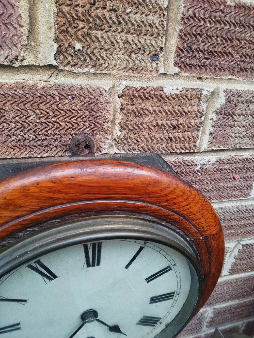 A circular late nineteenth-century oak dial wall clock featuring an off-white face with Roman numerals and a brass bezel. View II