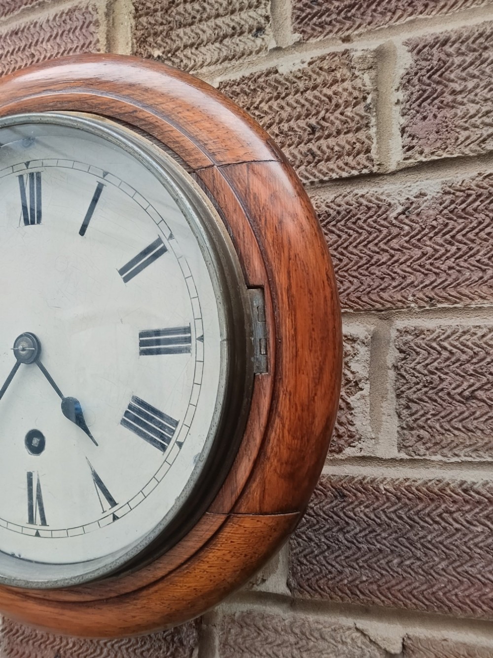 A circular late nineteenth-century oak dial wall clock featuring an off-white face with Roman numerals and a brass bezel. View V