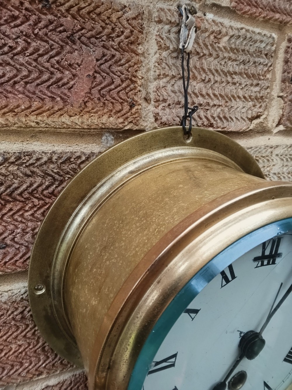 A circular antique brass marine bulkhead wall clock featuring a white dial with black Roman numerals and side latch fixtures. View III