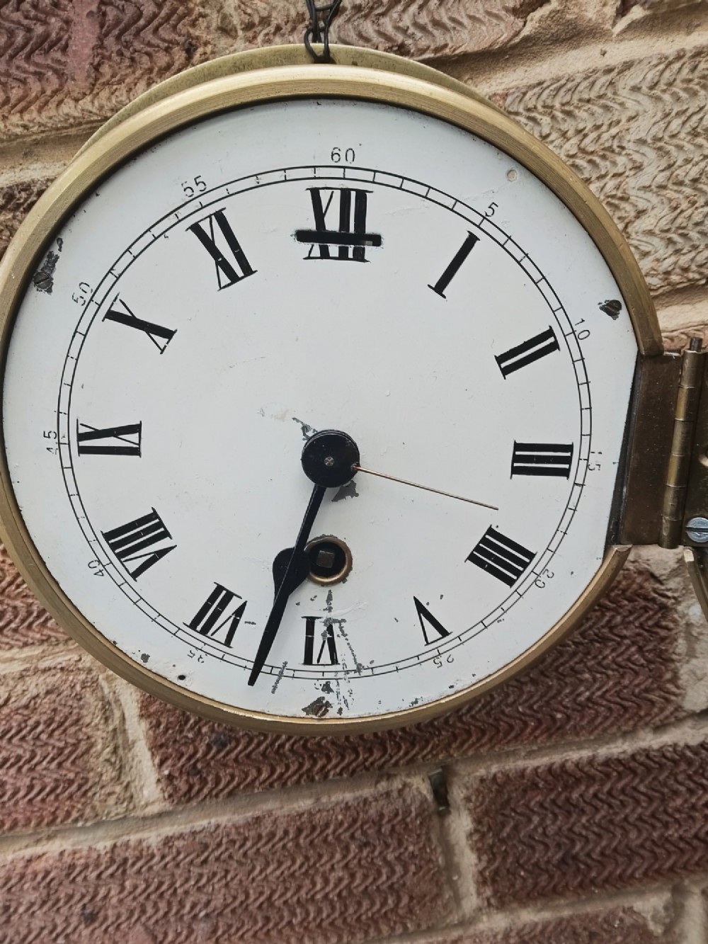 A circular antique brass marine bulkhead wall clock featuring a white dial with black Roman numerals and side latch fixtures. View VI