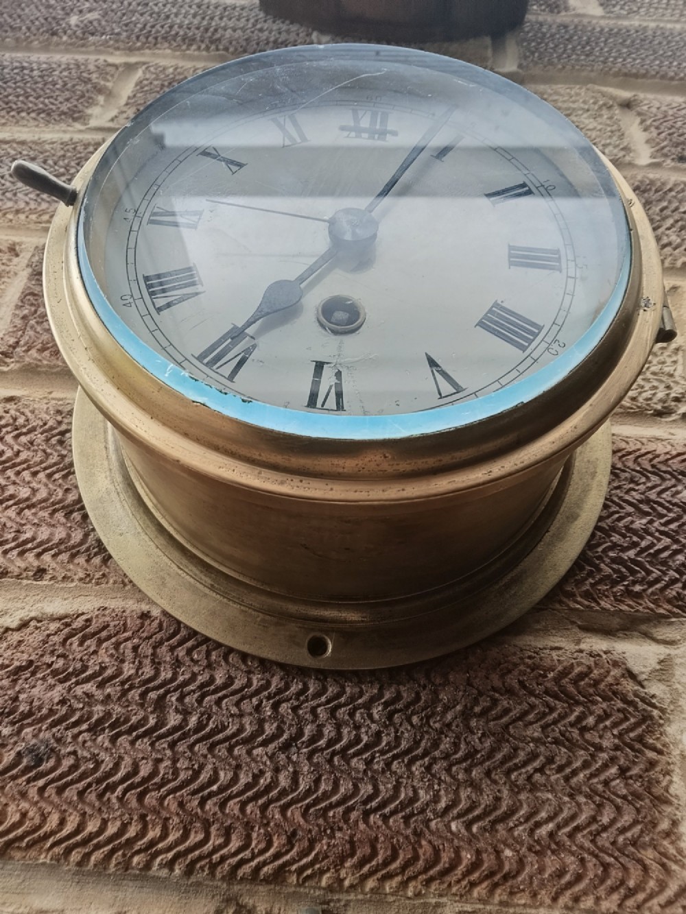 A circular antique brass marine bulkhead wall clock featuring a white dial with black Roman numerals and side latch fixtures. View VIII