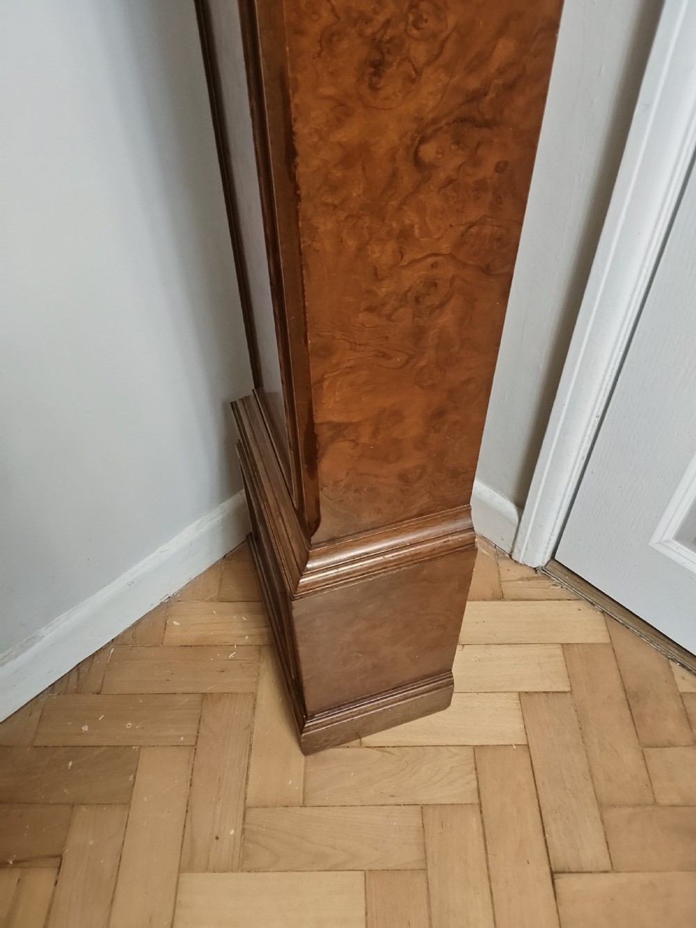 A freestanding burr walnut grandmother clock featuring an arched hood, brass dial with Roman numerals, and a figure-matched veneered trunk. View VI