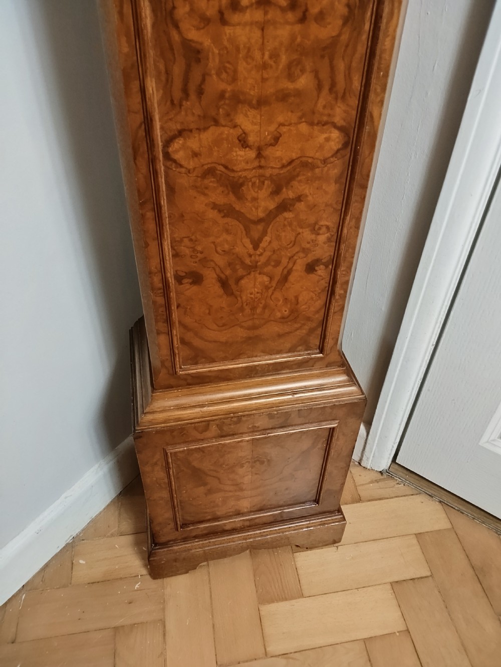 A freestanding burr walnut grandmother clock featuring an arched hood, brass dial with Roman numerals, and a figure-matched veneered trunk. View XII