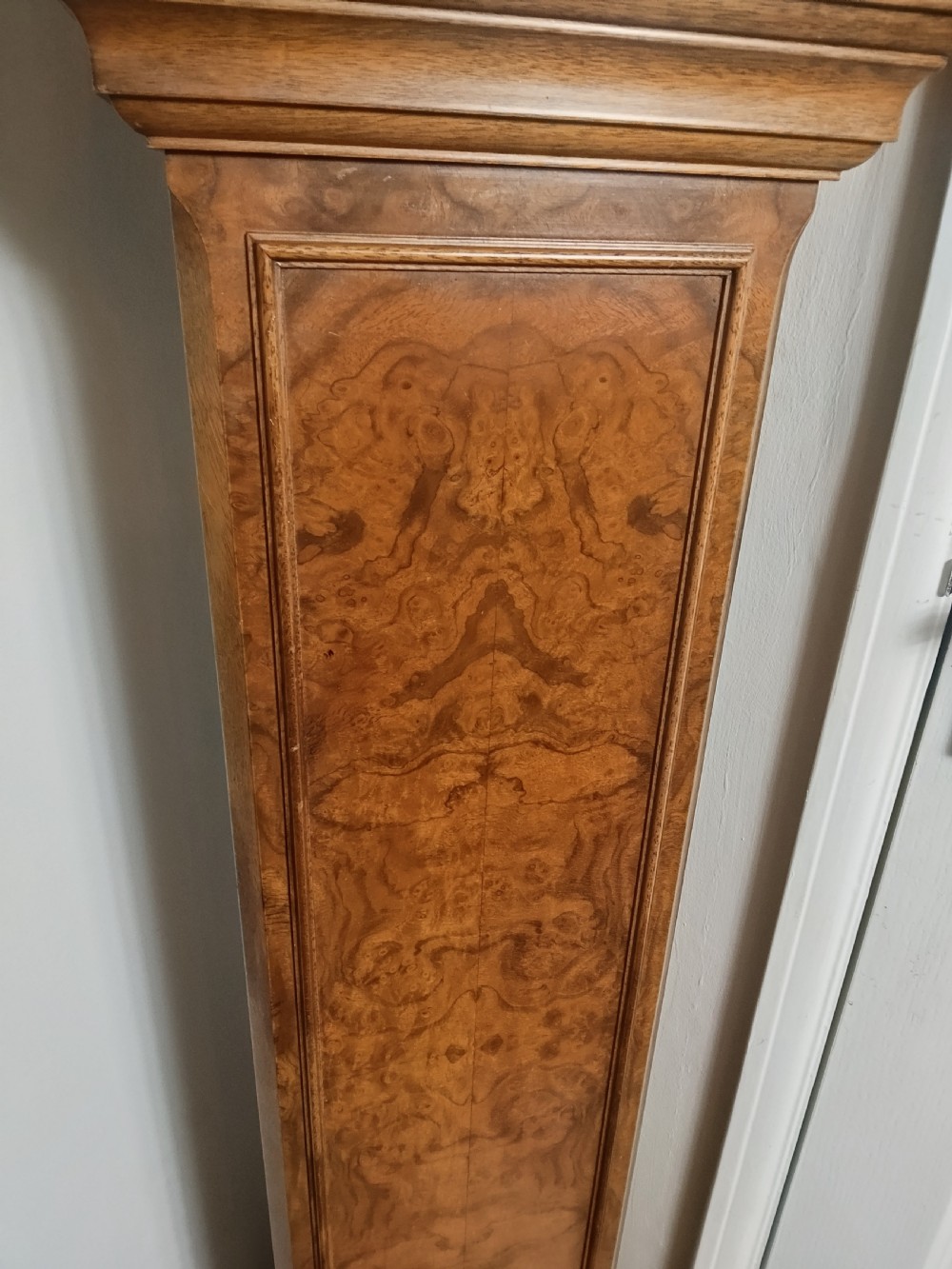 A freestanding burr walnut grandmother clock featuring an arched hood, brass dial with Roman numerals, and a figure-matched veneered trunk. View XIII