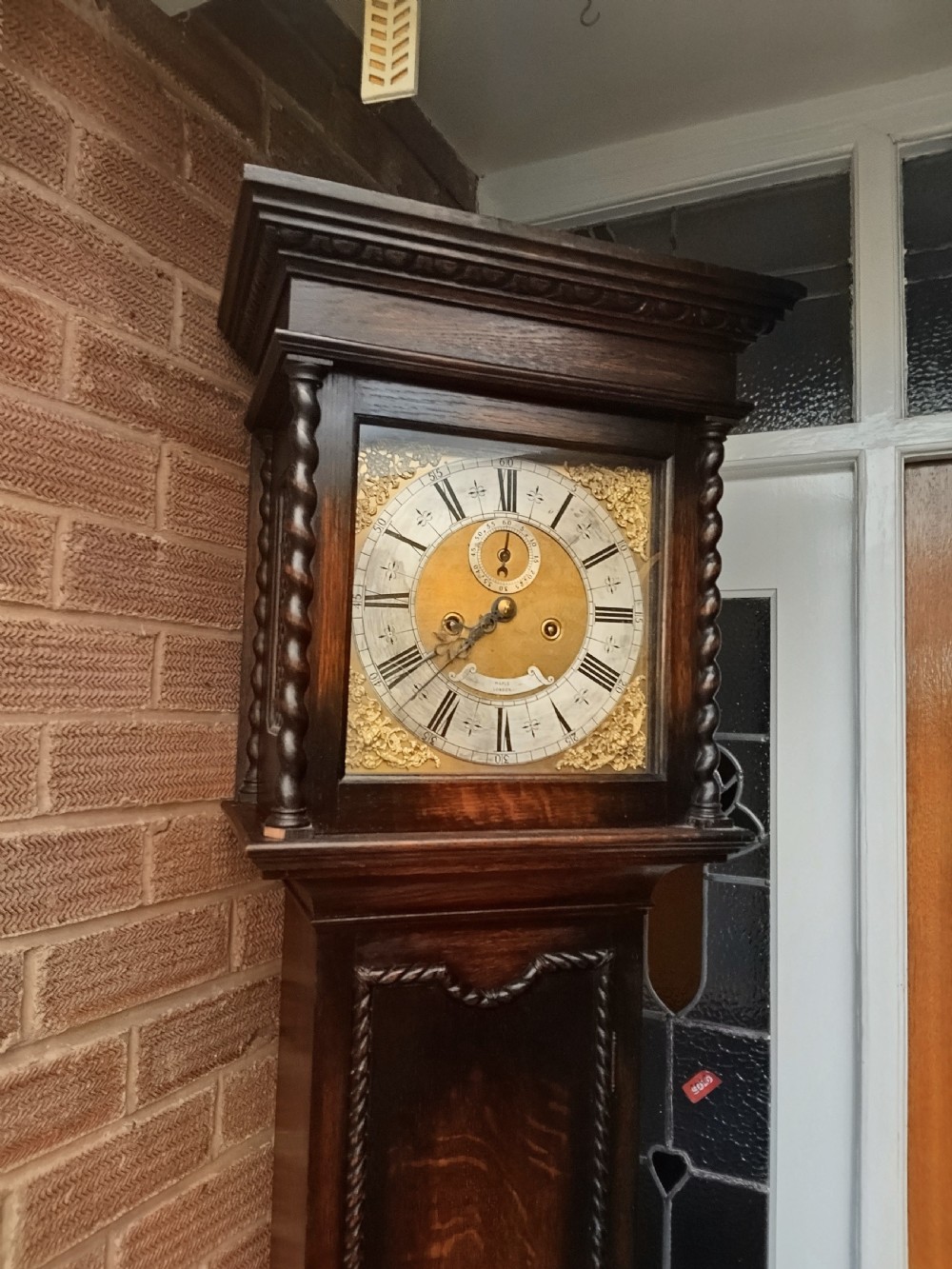 A tall dark oak longcase clock featuring rope twist columns, a square brass dial with silvered chapter ring, and a carved wooden casing. View II