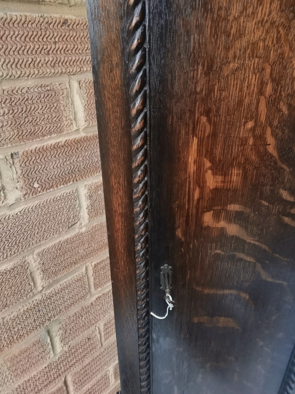 A tall dark oak longcase clock featuring rope twist columns, a square brass dial with silvered chapter ring, and a carved wooden casing. View IV