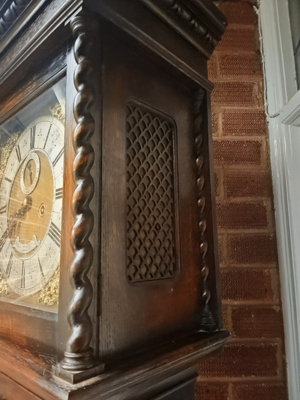 A tall dark oak longcase clock featuring rope twist columns, a square brass dial with silvered chapter ring, and a carved wooden casing. View VI