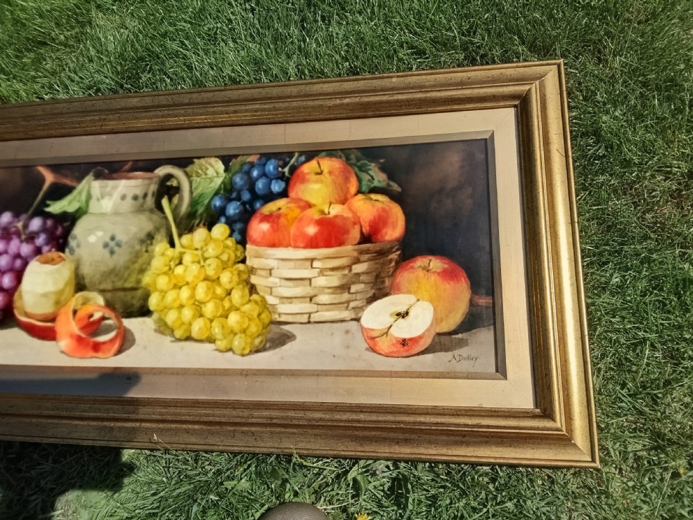 A wide framed watercolour painting depicting a still life arrangement of grapes, apples, a peeled fruit, a ceramic jug, and a woven basket. View II
