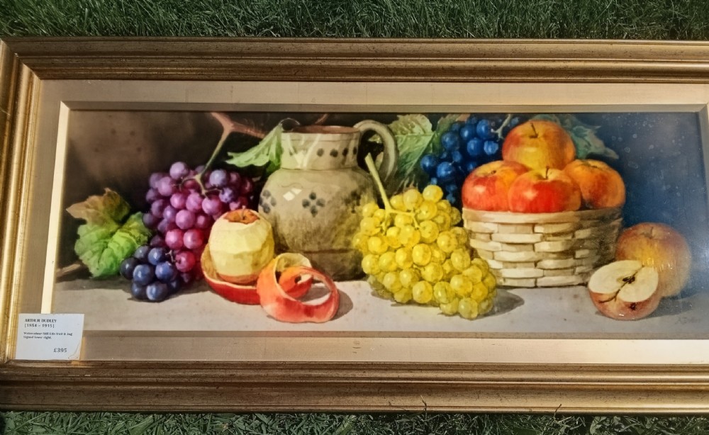 A wide framed watercolour painting depicting a still life arrangement of grapes, apples, a peeled fruit, a ceramic jug, and a woven basket. View III