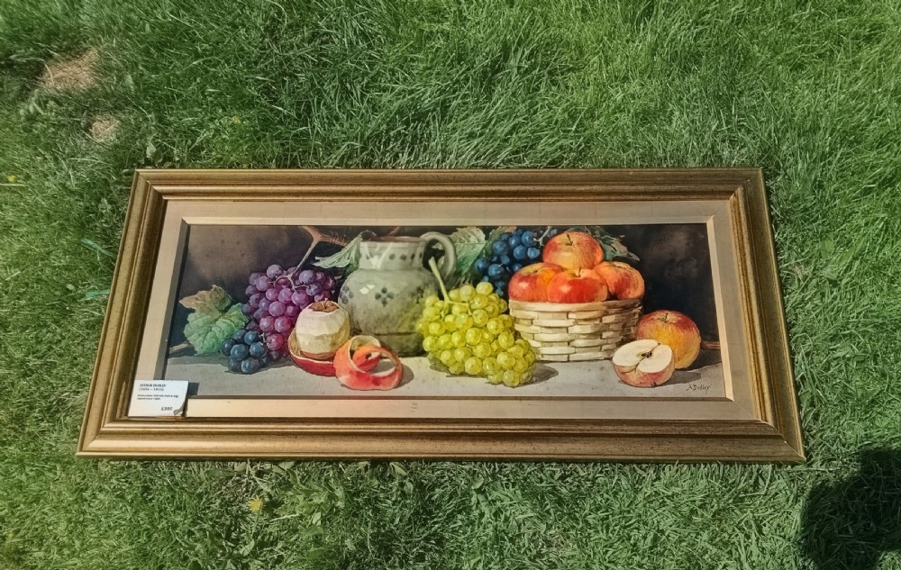 A wide framed watercolour painting depicting a still life arrangement of grapes, apples, a peeled fruit, a ceramic jug, and a woven basket. View V