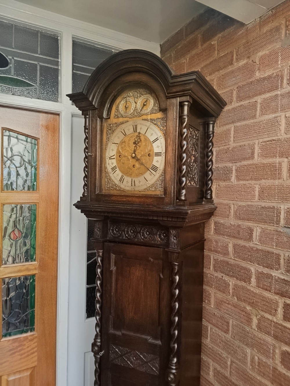 A tall dark oak longcase clock featuring an arched hood, barley twist columns, carved wood panels, and an ornate brass dial. View III