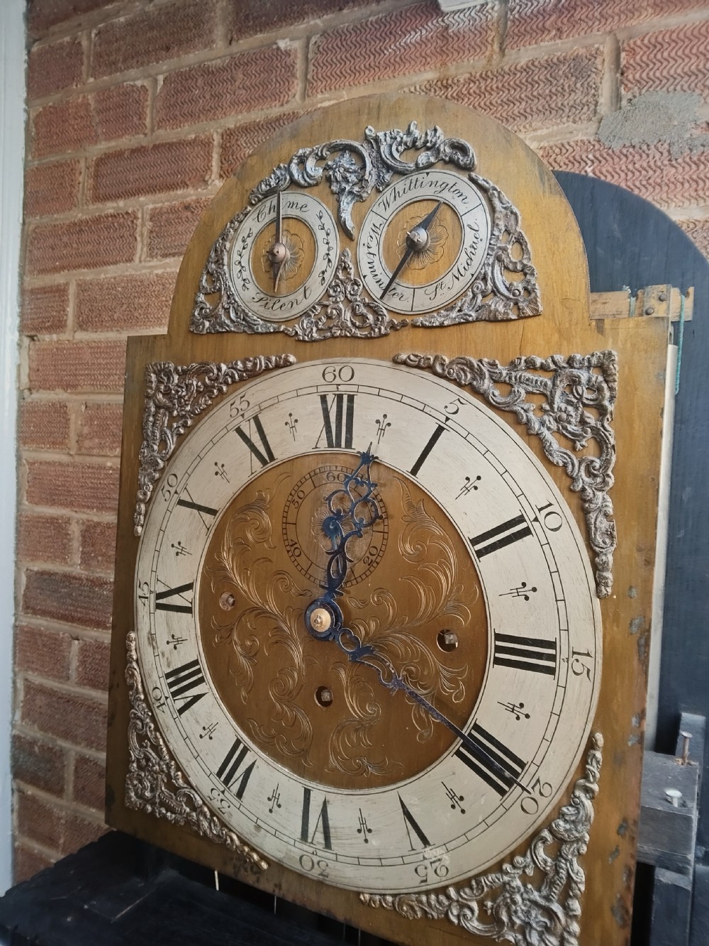 A tall dark oak longcase clock featuring an arched hood, barley twist columns, carved wood panels, and an ornate brass dial. View IX