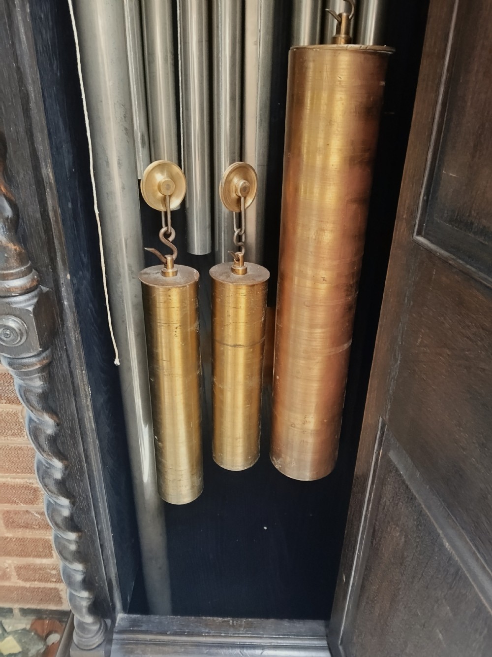 A tall dark oak longcase clock featuring an arched hood, barley twist columns, carved wood panels, and an ornate brass dial. View XII