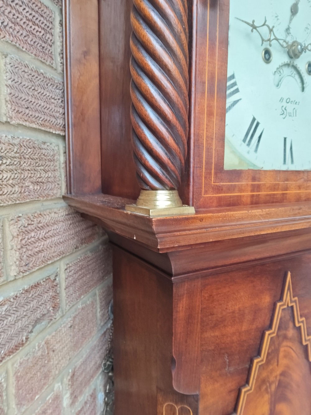 An antique flame mahogany longcase clock featuring a swan-neck pediment, brass finials, reeded columns, and a painted clock face with Roman numerals. View II