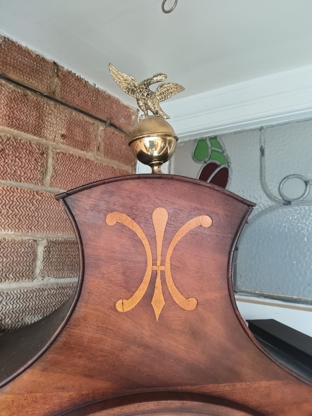 An antique flame mahogany longcase clock featuring a swan-neck pediment, brass finials, reeded columns, and a painted clock face with Roman numerals. View VIII
