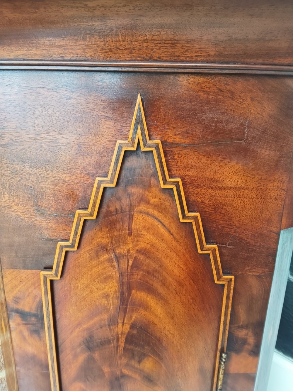An antique flame mahogany longcase clock featuring a swan-neck pediment, brass finials, reeded columns, and a painted clock face with Roman numerals. View X