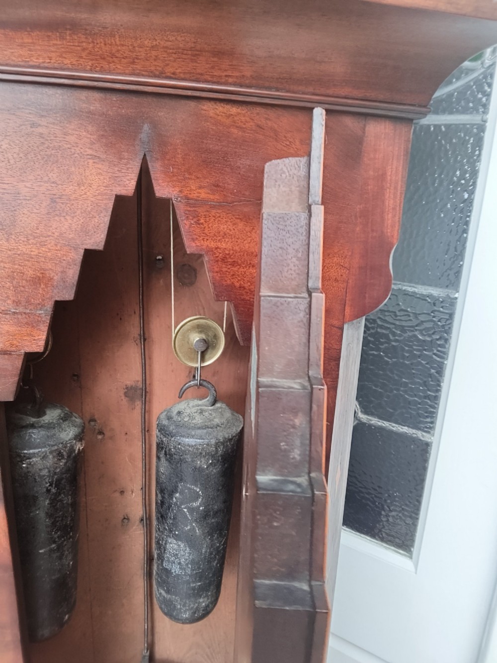 An antique flame mahogany longcase clock featuring a swan-neck pediment, brass finials, reeded columns, and a painted clock face with Roman numerals. View XI