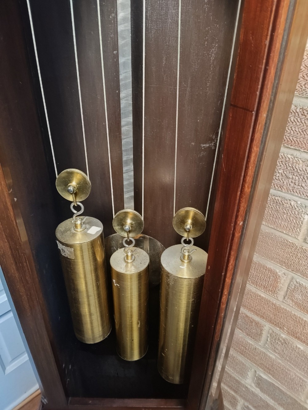 A tall wooden longcase clock featuring an arched hood, silvered brass dial, and a glazed door showcasing internal brass weights and pendulum. View V