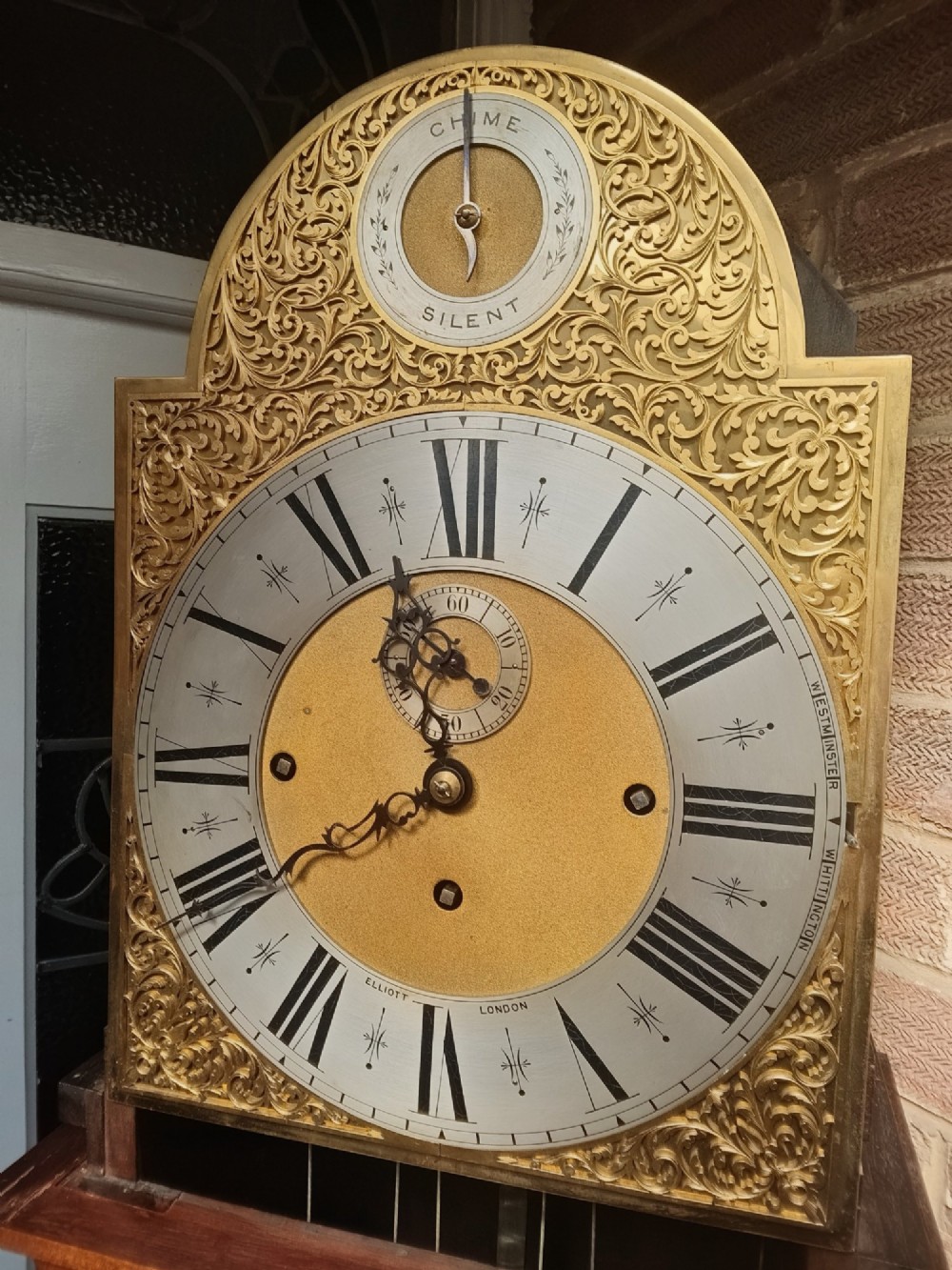 A tall wooden longcase clock featuring an arched hood, silvered brass dial, and a glazed door showcasing internal brass weights and pendulum. View VIII