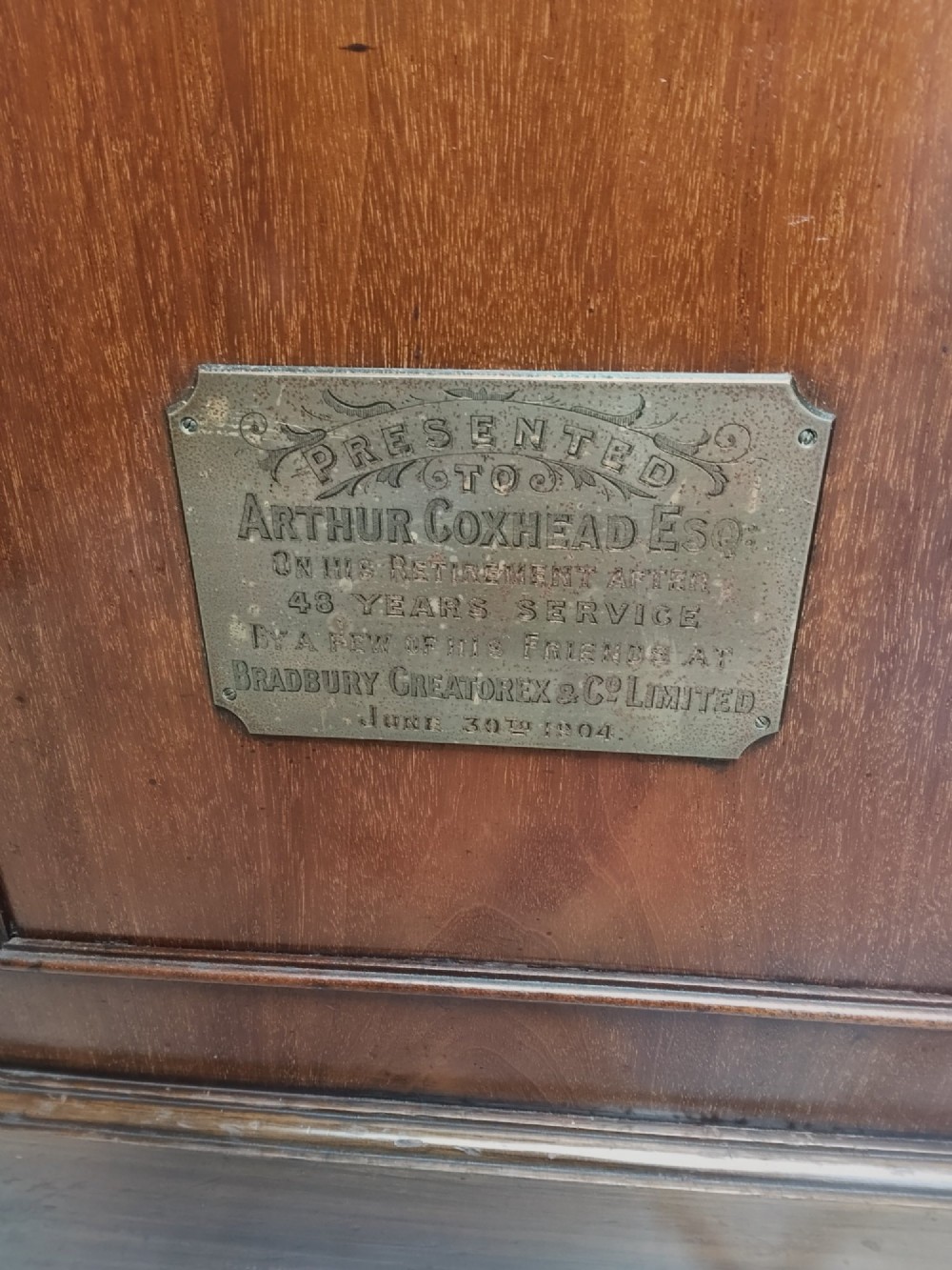 A tall wooden longcase clock featuring an arched hood, silvered brass dial, and a glazed door showcasing internal brass weights and pendulum. View IX