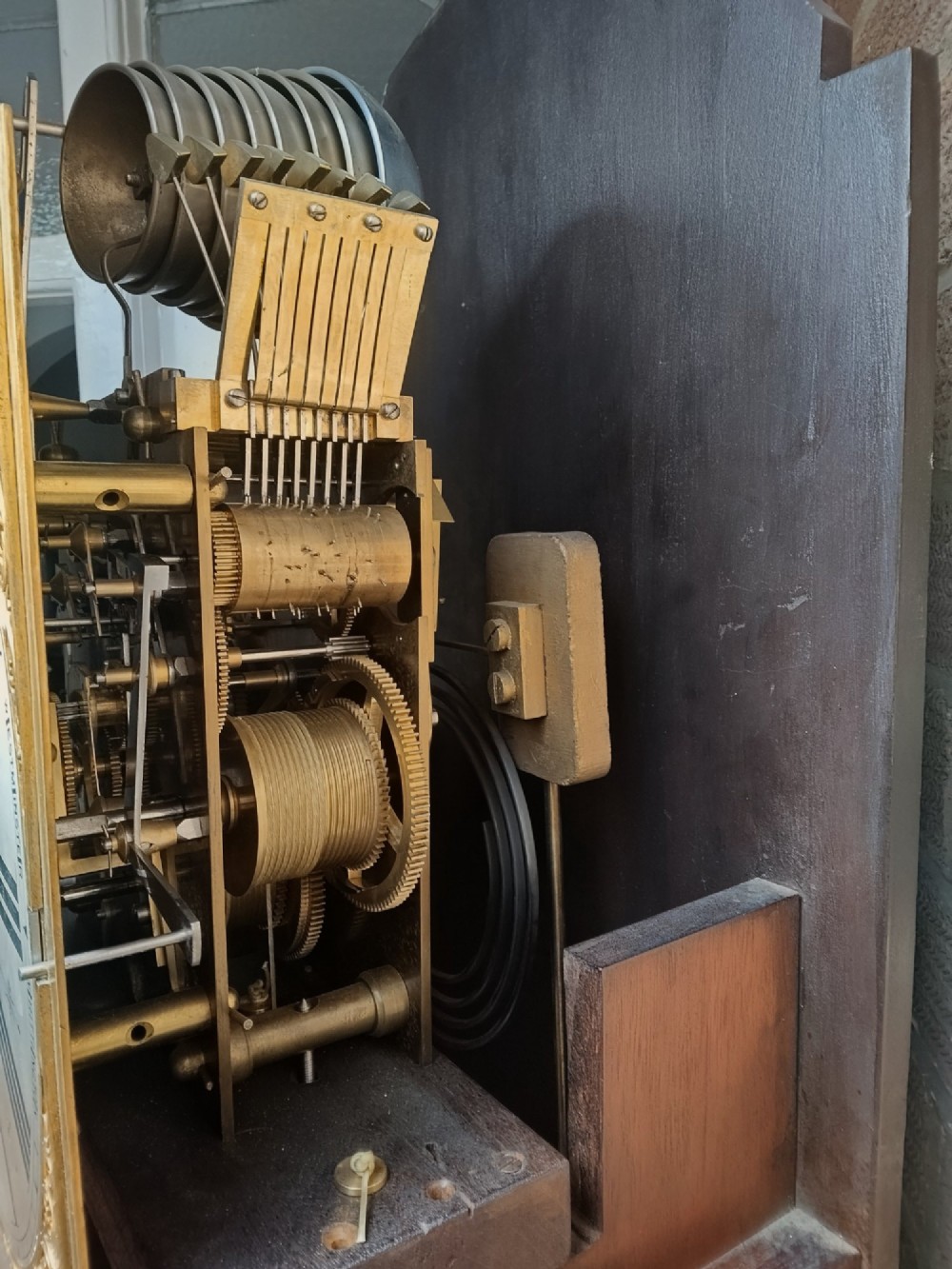 A tall wooden longcase clock featuring an arched hood, silvered brass dial, and a glazed door showcasing internal brass weights and pendulum. View X