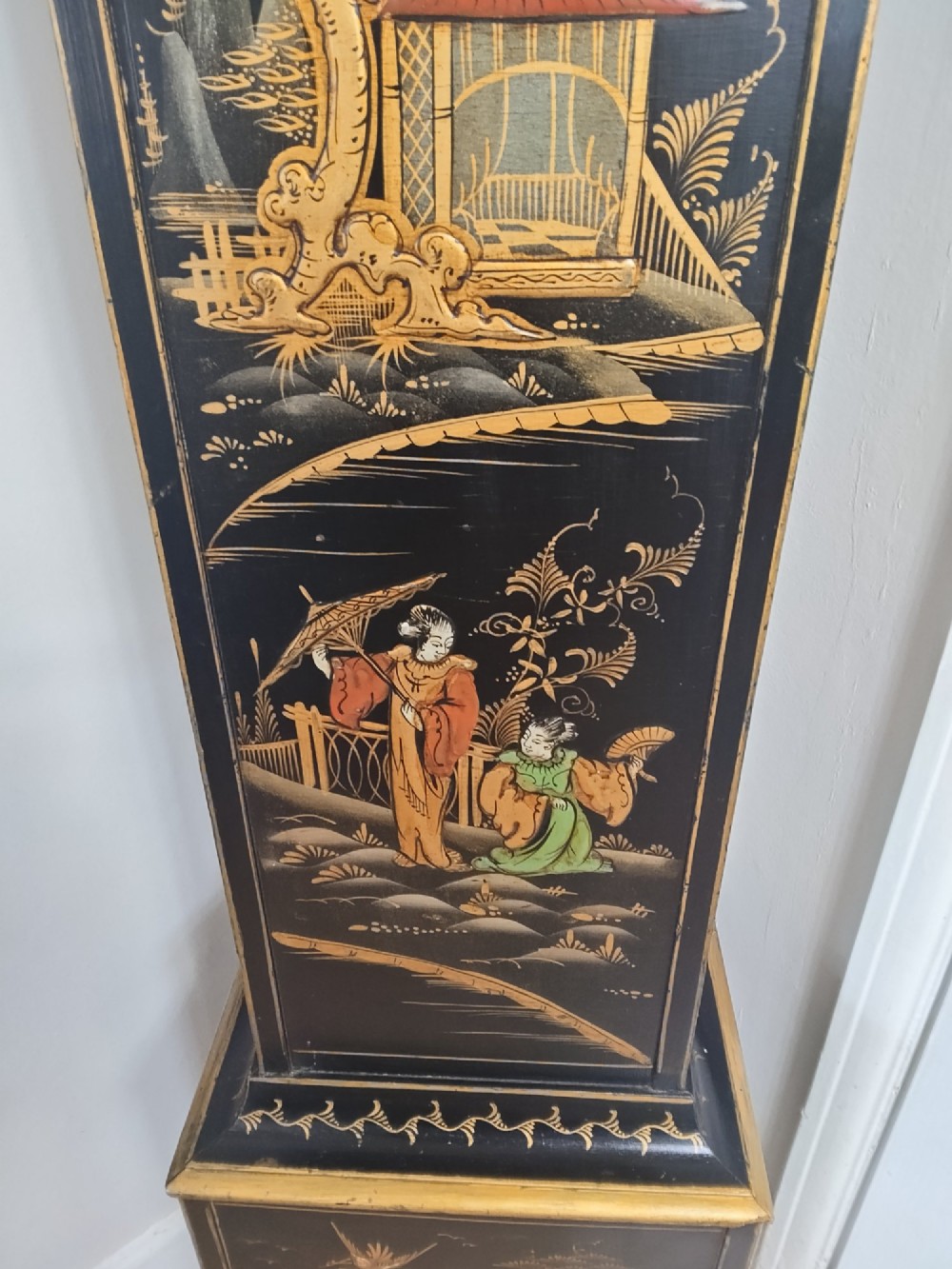 A slender black lacquer grandmother clock decorated with gilded chinoiserie landscape motifs and fitted with an arched brass dial. View III