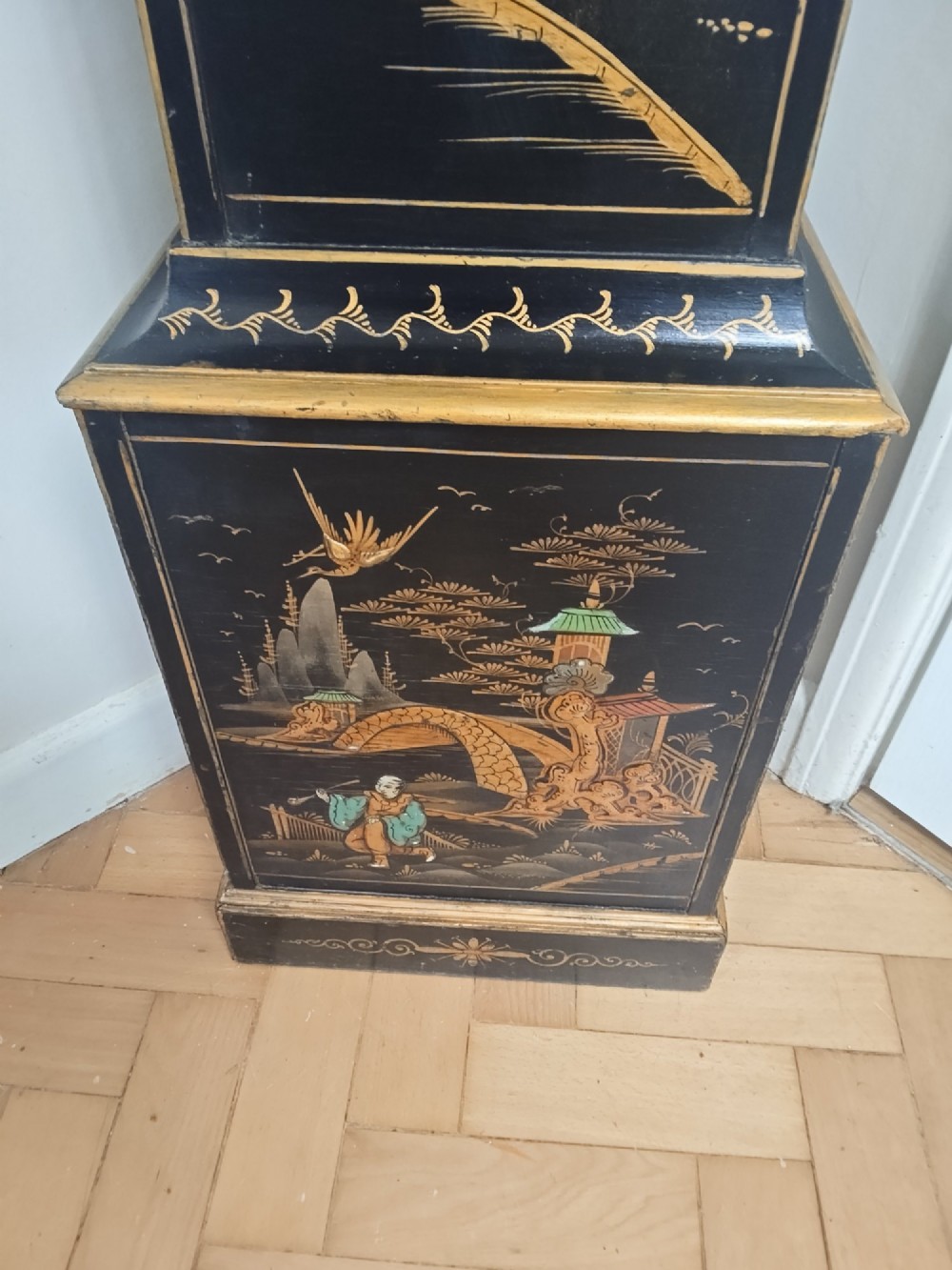 A slender black lacquer grandmother clock decorated with gilded chinoiserie landscape motifs and fitted with an arched brass dial. View IV