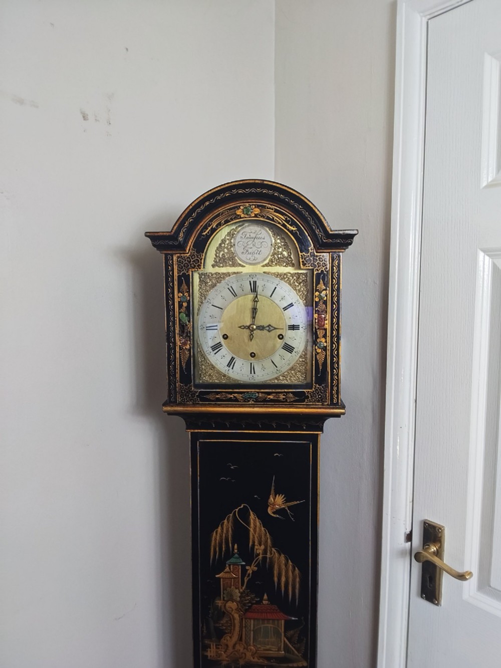 A slender black lacquer grandmother clock decorated with gilded chinoiserie landscape motifs and fitted with an arched brass dial. View IX