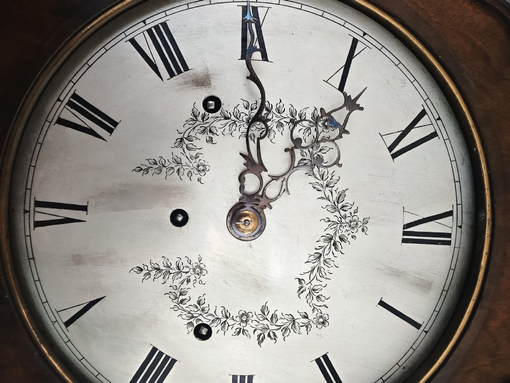 A slim burr walnut grandmother longcase clock featuring an arched hood, round silvered dial, and bookmatched timber grain. View VI
