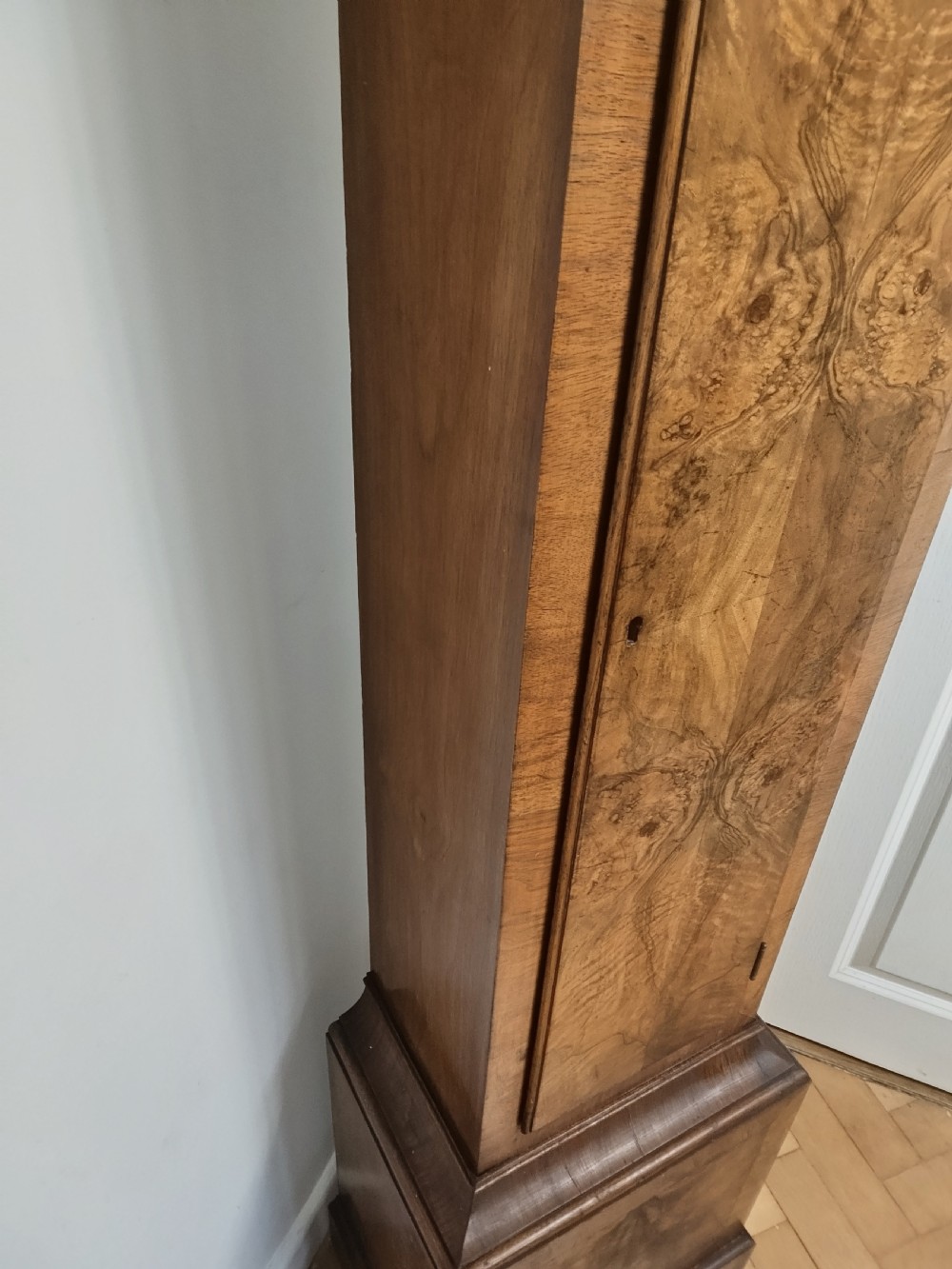 A slim burr walnut grandmother longcase clock featuring an arched hood, round silvered dial, and bookmatched timber grain. View VIII