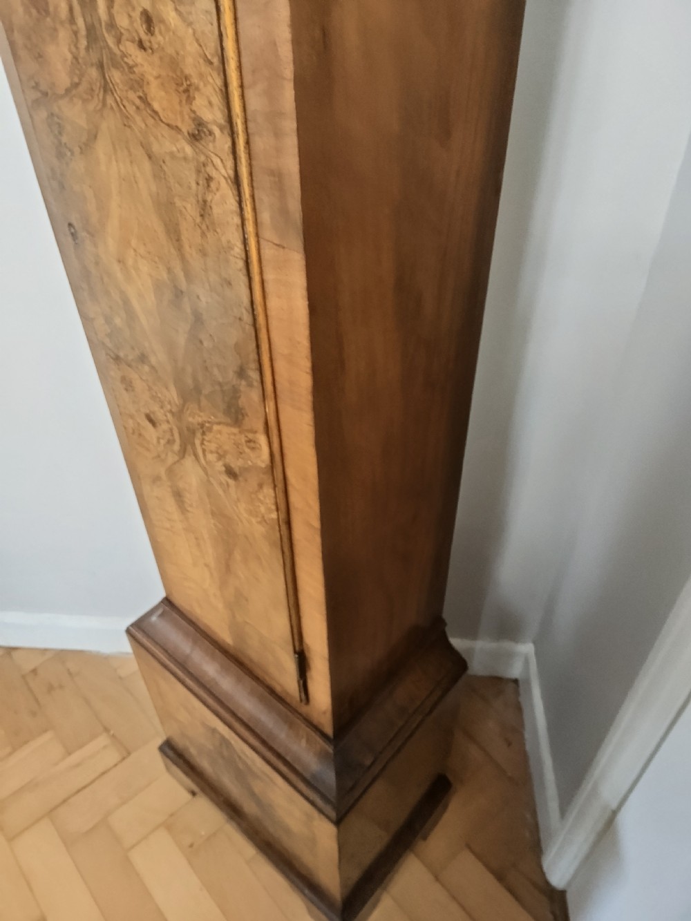 A slim burr walnut grandmother longcase clock featuring an arched hood, round silvered dial, and bookmatched timber grain. View IX