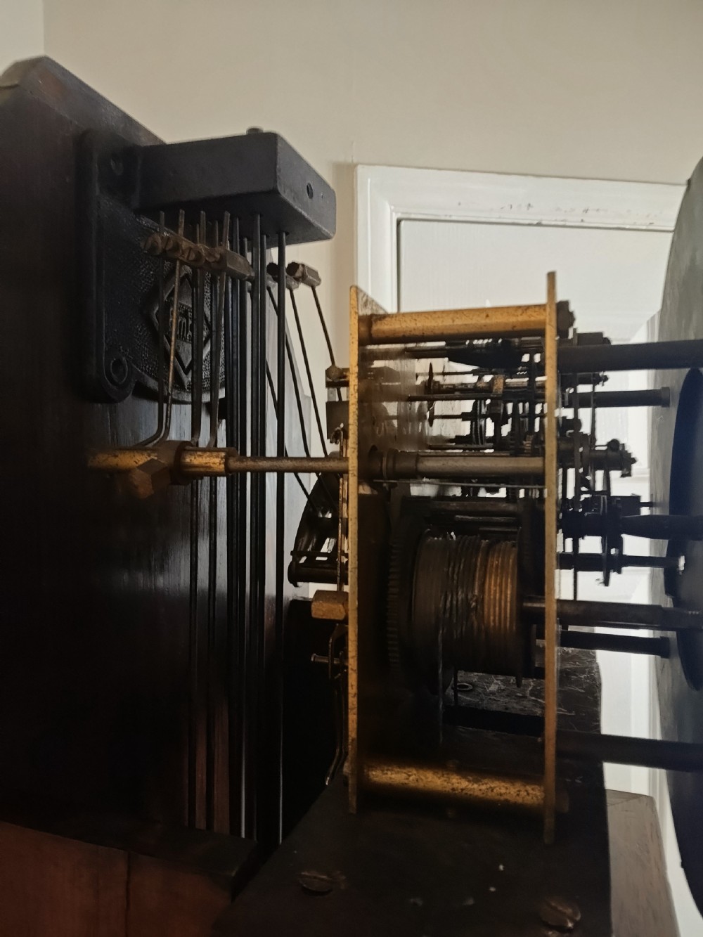 A slim burr walnut grandmother longcase clock featuring an arched hood, round silvered dial, and bookmatched timber grain. View XII