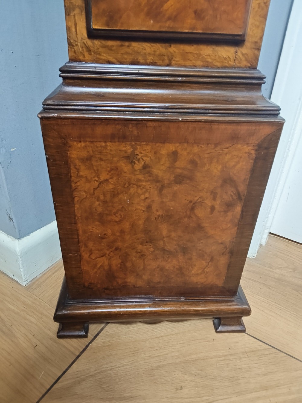 A tall slim figured walnut grandmother longcase clock featuring an arched hood, brass and silvered dial, and a polished wood trunk. View V