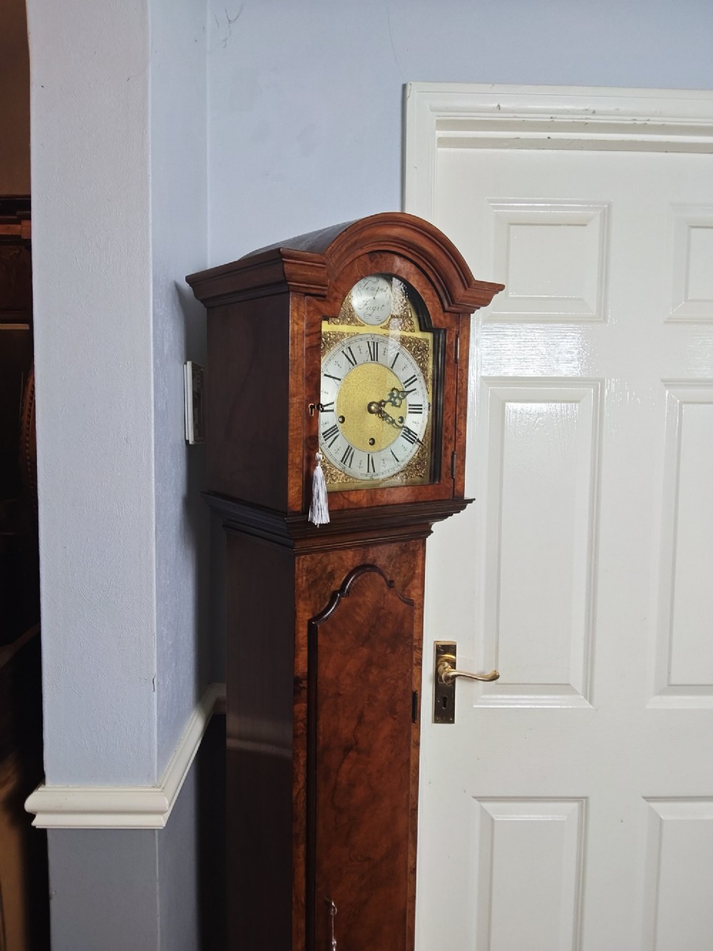 A tall slim figured walnut grandmother longcase clock featuring an arched hood, brass and silvered dial, and a polished wood trunk. View XIV