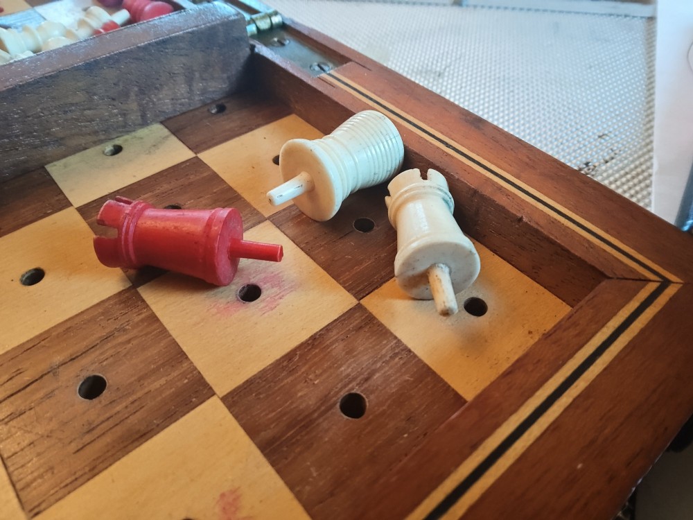 An open antique mahogany folding travelling chess board containing miniature carved red and natural white bone chess pieces fitted into individual pegged holes. View II
